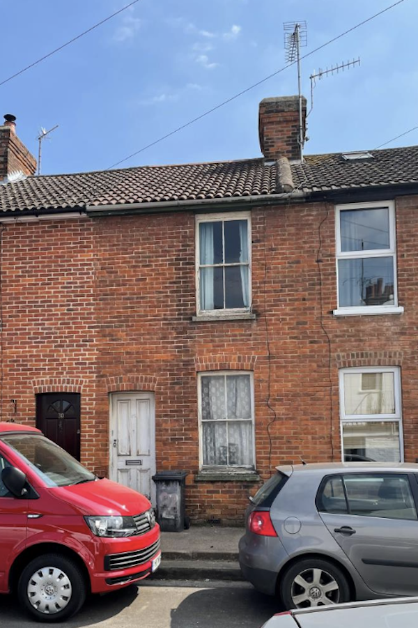 'A red van and a grey car are parked outside Lot 1, a two-bedroom house