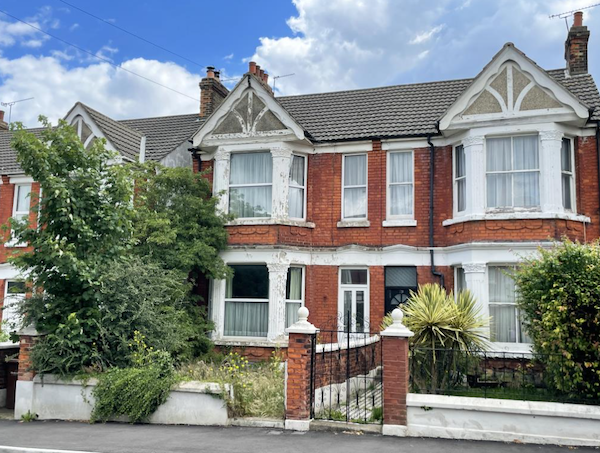 A large, semi-detached house with white facades and plenty of greenery is pictured