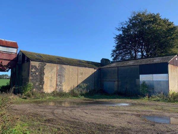 A flat expanse of muddy ground gives rise to an L-shaped detached grain store