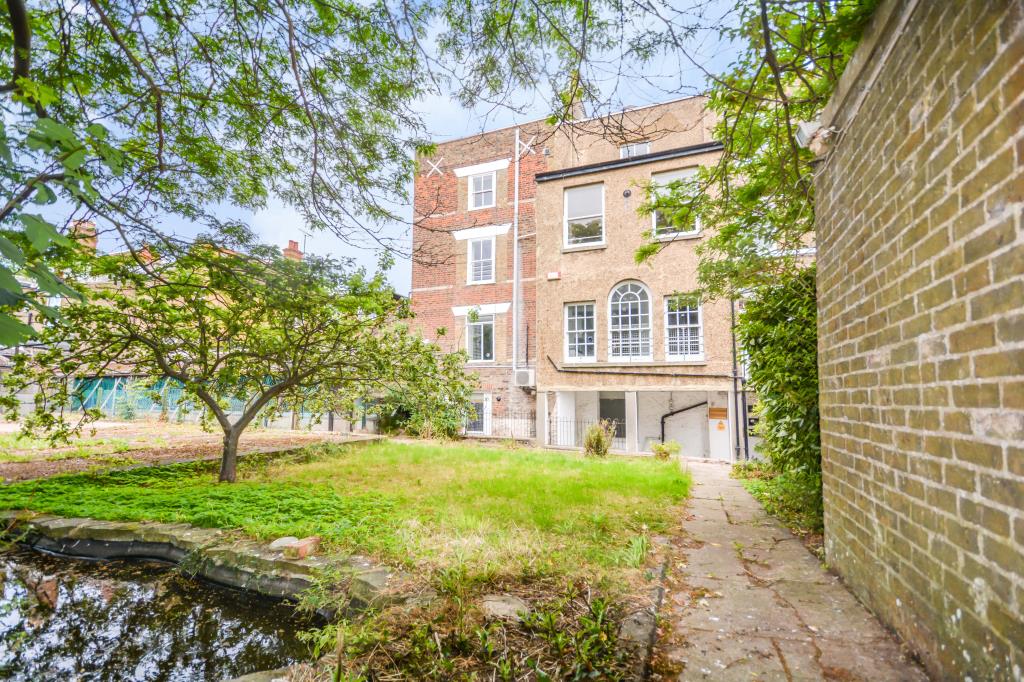 Lot 64, a four storey period property with a blue front door stands next to vivid green trees and another brick building