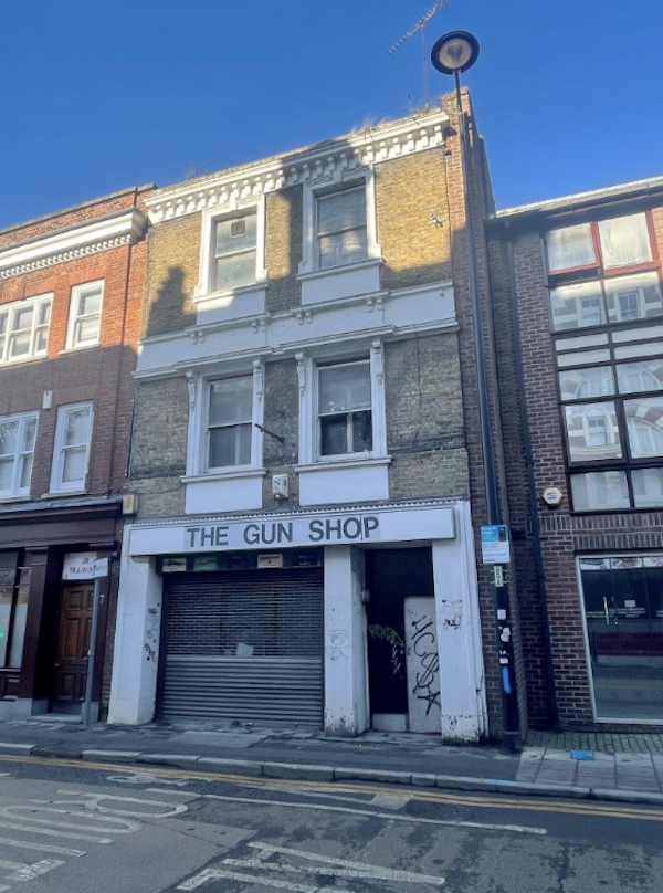 The words 'The Gun Shop" are written on a shopfront which sits underneath a maisonette on a high street
