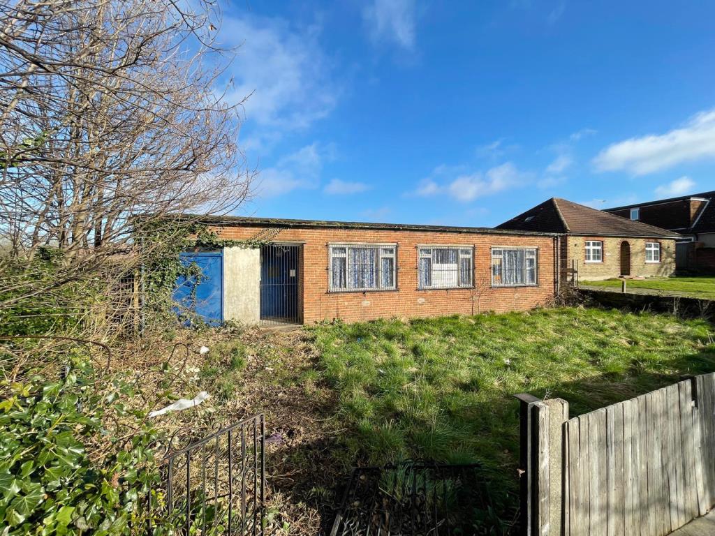 Lot 80, a former scout hut, is pictured behind a wooden fence with a grass verge against clear skies