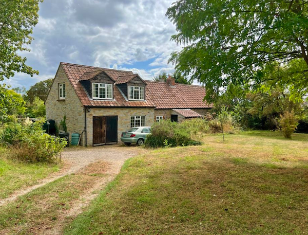 A large barn conversion sits among trees with a silver car on the driveway