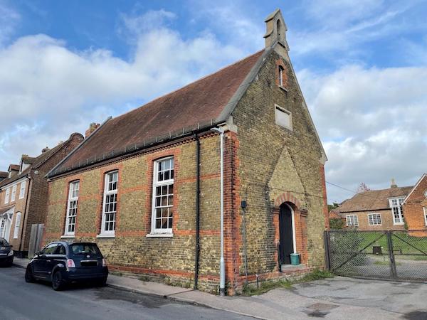 A side view of a former brick school with large windows and a central door